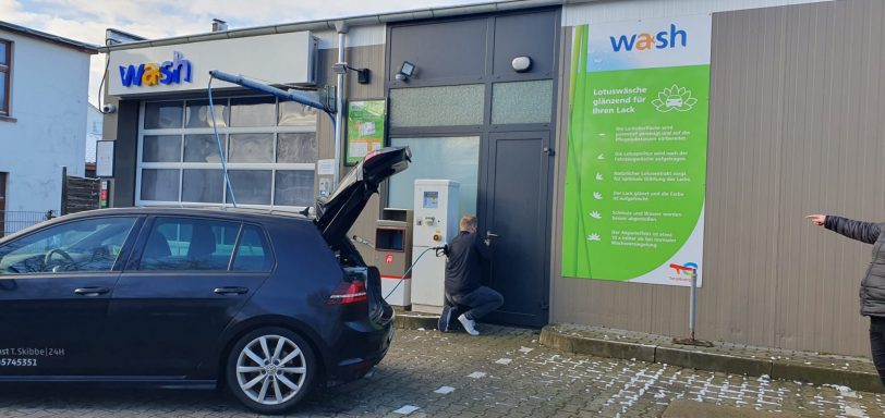 Ein schwarzes Auto steht vor einem Gebäude mit einem großen grünen Schild.